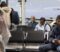 Busy airport terminal filled with people traveling by plane, scrolling on smartphones. Diverse travelers using mobile phones while sitting in departure hub waiting area, waiting for boarding