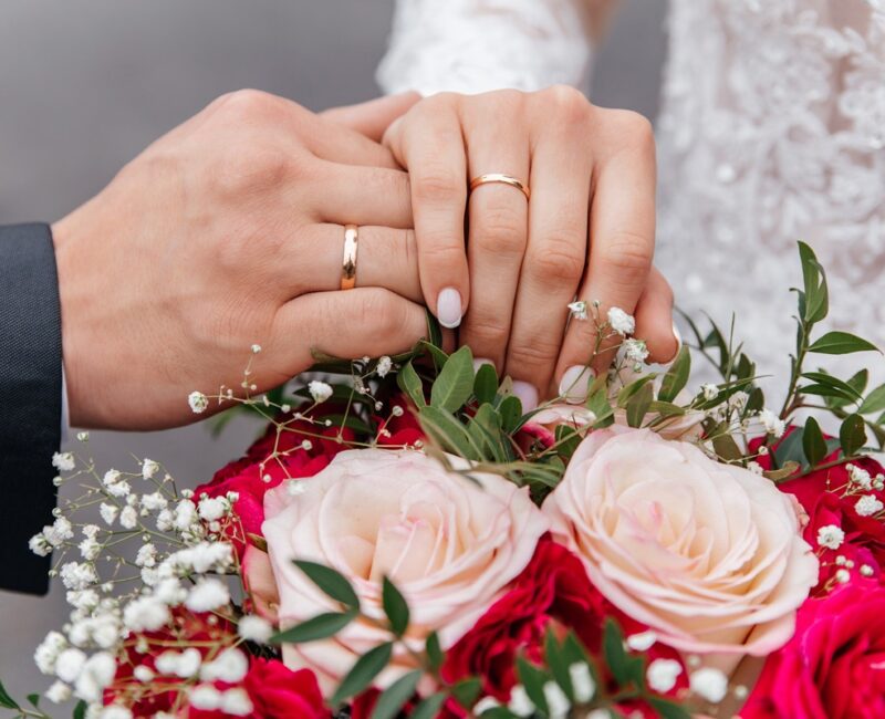 The hands of the bride and groom with rings on the background of a wedding bouquet of roses. The concept of marriage.