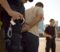 Patrol officers team arresting male offender on city street. Policewoman reporting to police station by radio while policeman putting handcuffs on hands of violator